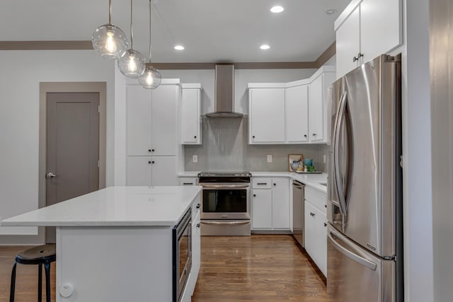 kitchen with pendant lighting, stainless steel appliances, a center island, white cabinets, and wall chimney exhaust hood