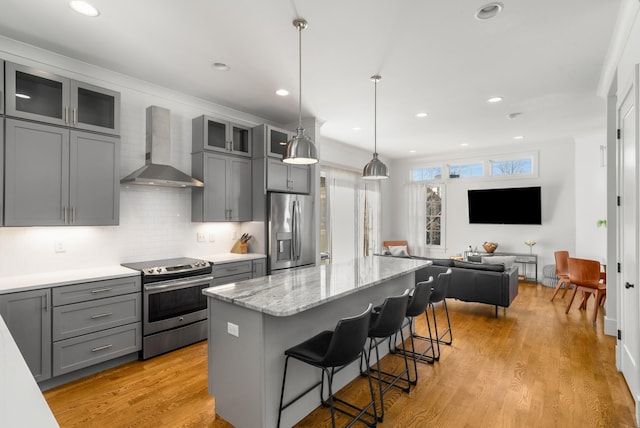 kitchen with wall chimney range hood, a breakfast bar, appliances with stainless steel finishes, a center island, and light hardwood / wood-style floors