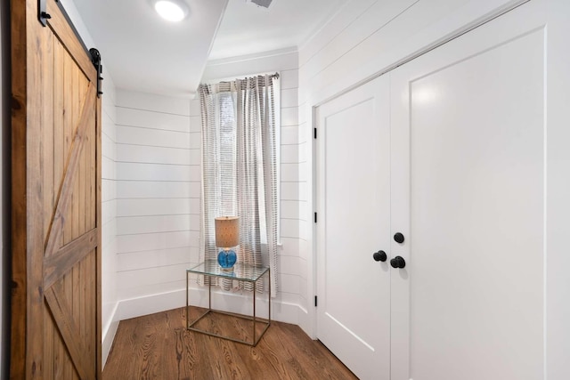 entryway featuring a barn door, dark wood-type flooring, and wood walls