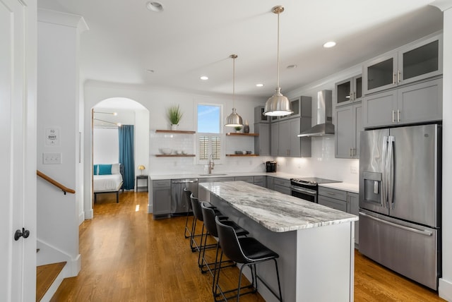 kitchen with pendant lighting, gray cabinets, appliances with stainless steel finishes, a kitchen island, and wall chimney exhaust hood