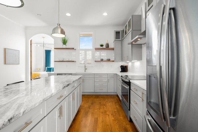 kitchen featuring appliances with stainless steel finishes, dark hardwood / wood-style floors, decorative backsplash, hanging light fixtures, and light stone countertops