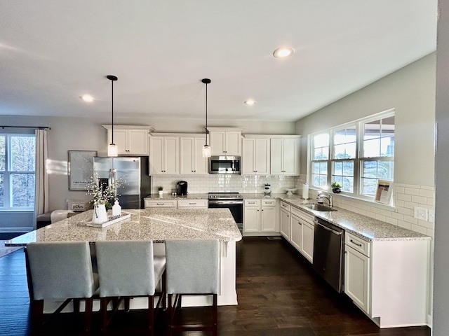 kitchen with a sink, stainless steel appliances, a kitchen island, and light stone countertops