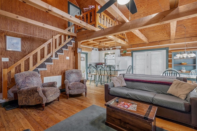 living room with light hardwood / wood-style flooring, wooden walls, ceiling fan, and a high ceiling