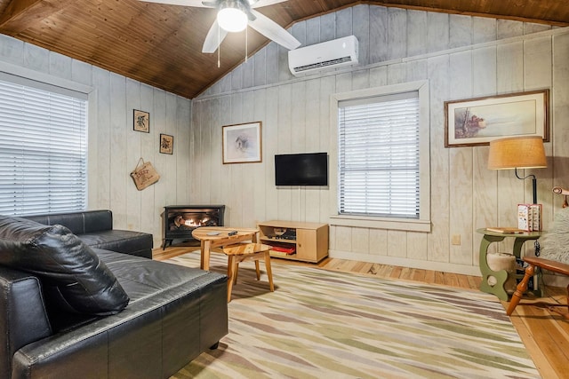 living room featuring vaulted ceiling, a wood stove, a wall mounted AC, and light wood-type flooring