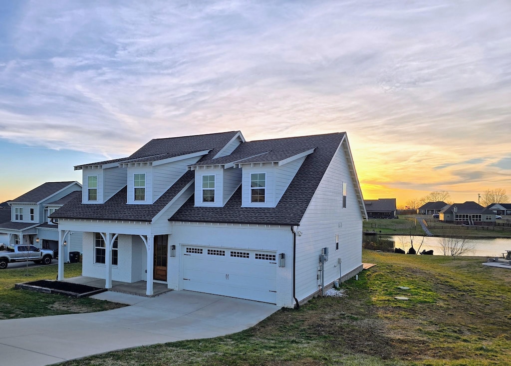 view of front of home with a yard, a garage, a porch, and a water view