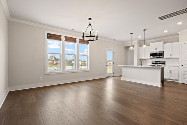 kitchen with appliances with stainless steel finishes, tasteful backsplash, white cabinetry, hanging light fixtures, and a center island with sink