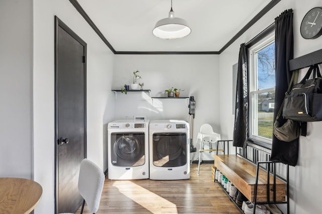 clothes washing area with crown molding, washing machine and dryer, and hardwood / wood-style floors