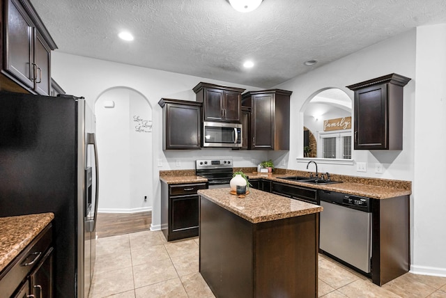 kitchen with light tile patterned flooring, dark brown cabinetry, sink, a kitchen island, and stainless steel appliances