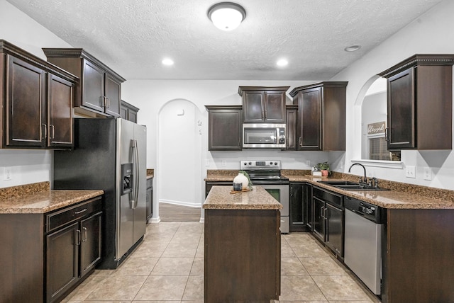 kitchen featuring sink, light tile patterned floors, appliances with stainless steel finishes, a center island, and dark brown cabinetry