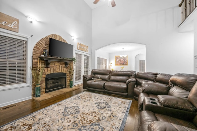 living room with a high ceiling, dark hardwood / wood-style floors, ceiling fan with notable chandelier, and a fireplace