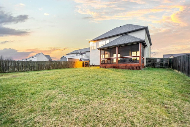 back house at dusk with a lawn and a sunroom