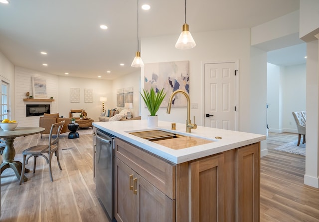 kitchen with decorative light fixtures, dishwasher, sink, a kitchen island with sink, and light hardwood / wood-style floors