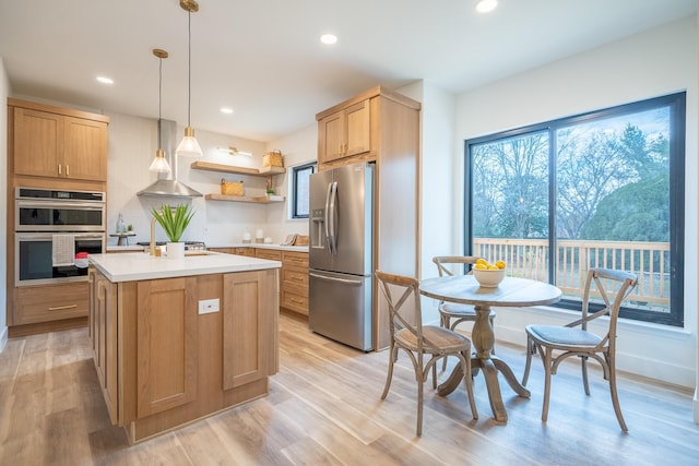 kitchen featuring pendant lighting, a kitchen island with sink, stainless steel appliances, wall chimney exhaust hood, and light wood-type flooring