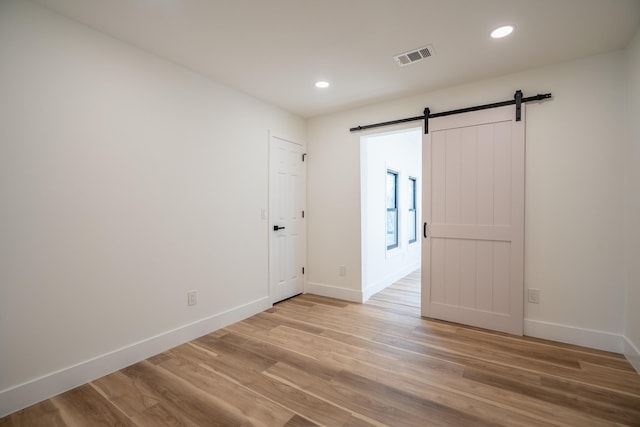 spare room with a barn door and light hardwood / wood-style floors