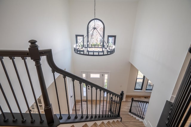 stairs with wood-type flooring, a chandelier, and a high ceiling