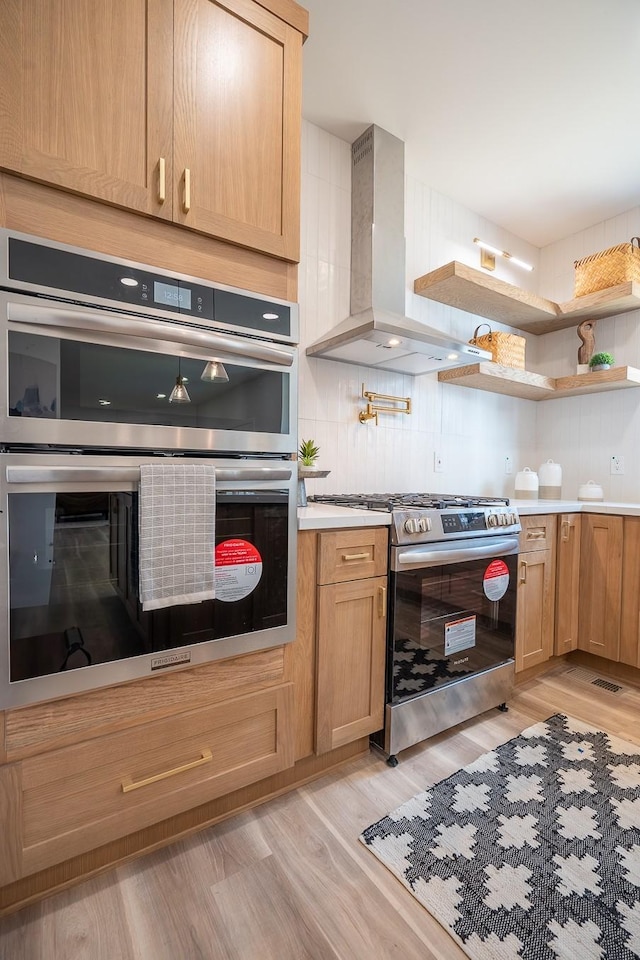 kitchen featuring wall chimney exhaust hood, stainless steel appliances, light hardwood / wood-style floors, and decorative backsplash