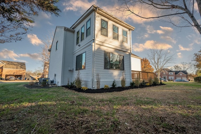 property exterior at dusk with a yard, a deck, and central air condition unit