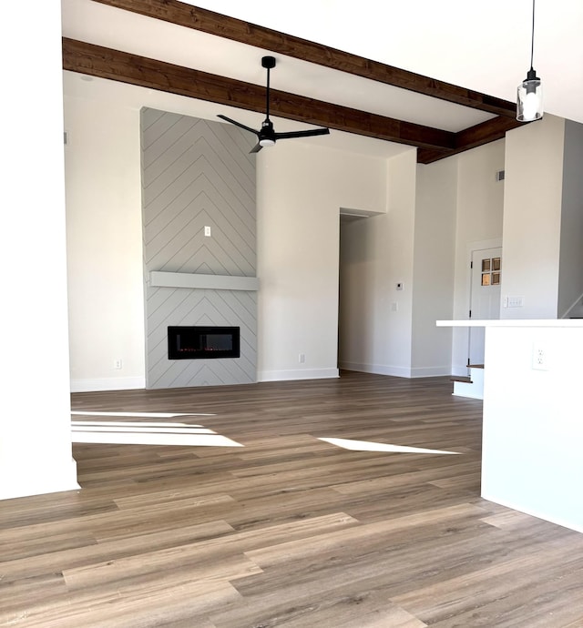 unfurnished living room with beamed ceiling, light hardwood / wood-style flooring, a large fireplace, and ceiling fan