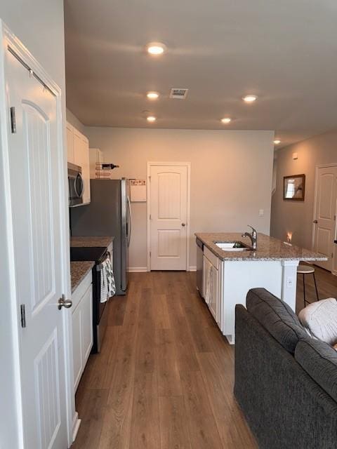 kitchen with sink, appliances with stainless steel finishes, a kitchen island with sink, white cabinets, and dark hardwood / wood-style flooring