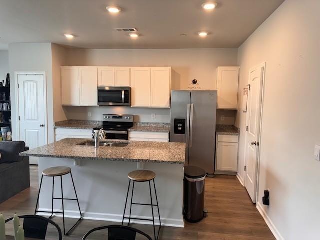 kitchen with white cabinetry, dark wood-type flooring, stainless steel appliances, and an island with sink