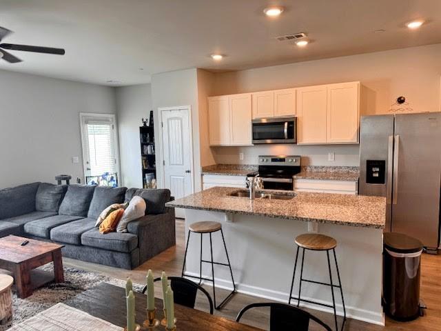 kitchen with white cabinetry, light stone counters, stainless steel appliances, and a center island with sink