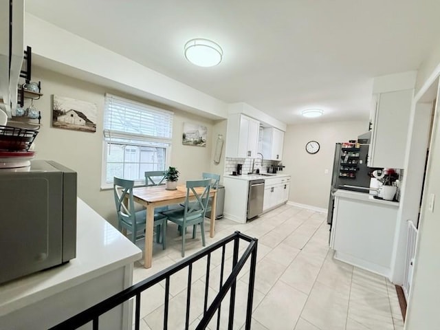 kitchen featuring tasteful backsplash, white cabinetry, dishwasher, sink, and light tile patterned floors