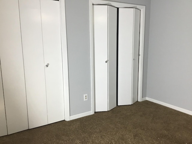 unfurnished bedroom featuring two closets and dark carpet