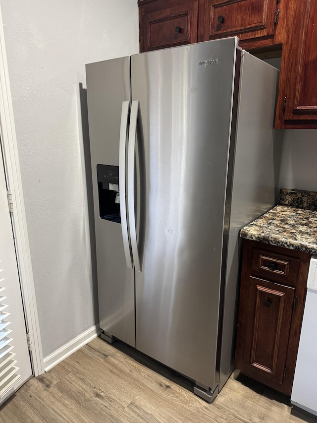 kitchen with dark stone countertops, white dishwasher, light hardwood / wood-style flooring, and stainless steel refrigerator with ice dispenser