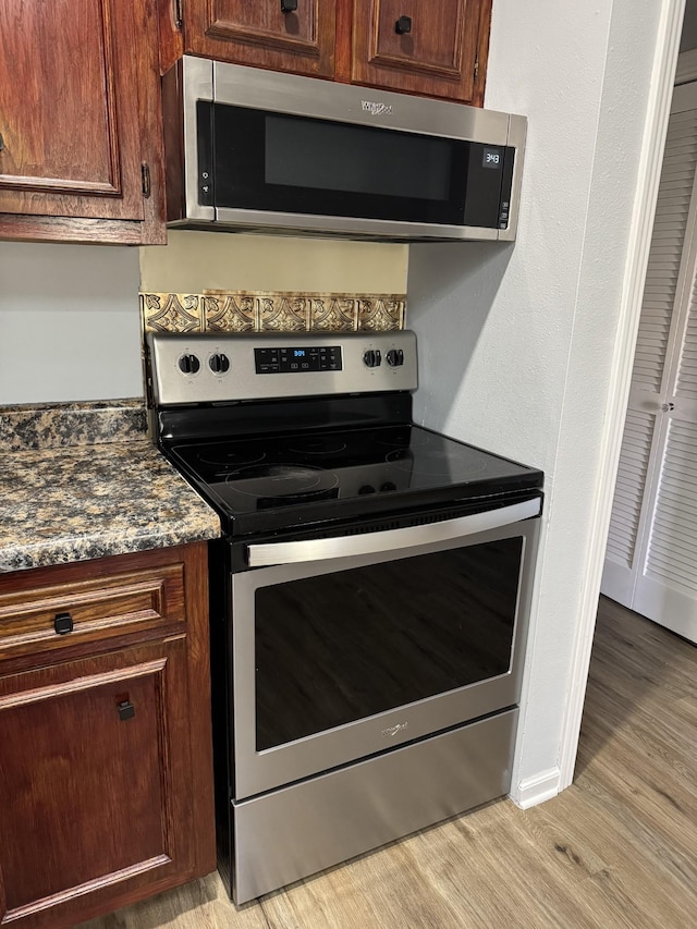 kitchen with appliances with stainless steel finishes, light wood-type flooring, and dark stone counters