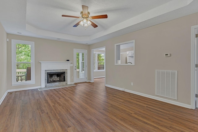 unfurnished living room featuring ceiling fan, a high end fireplace, a tray ceiling, and dark hardwood / wood-style flooring