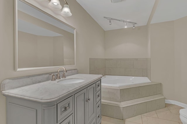 bathroom featuring tiled tub, vanity, track lighting, and toilet