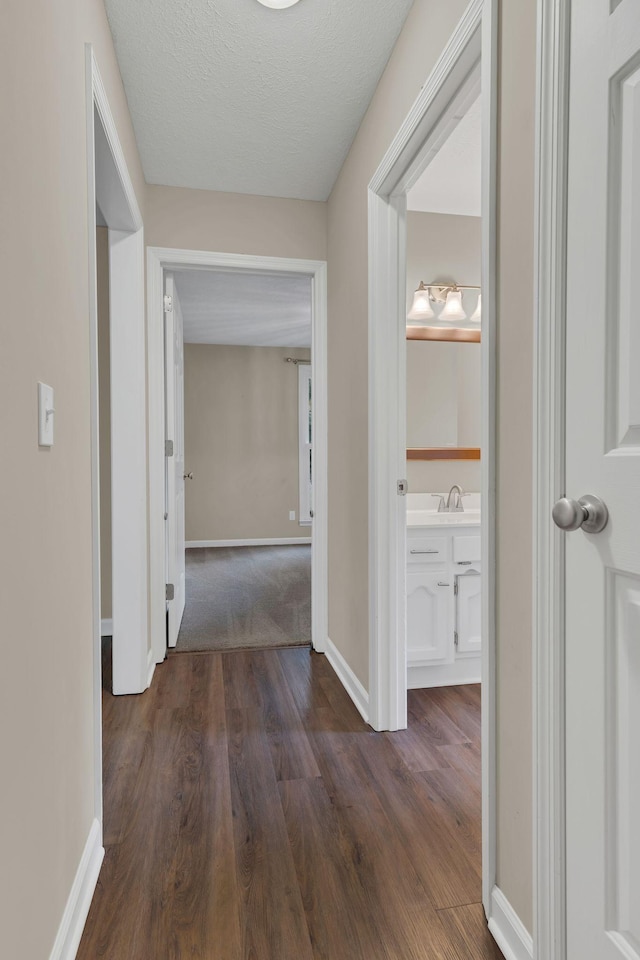 hallway featuring sink, dark wood-type flooring, and a textured ceiling