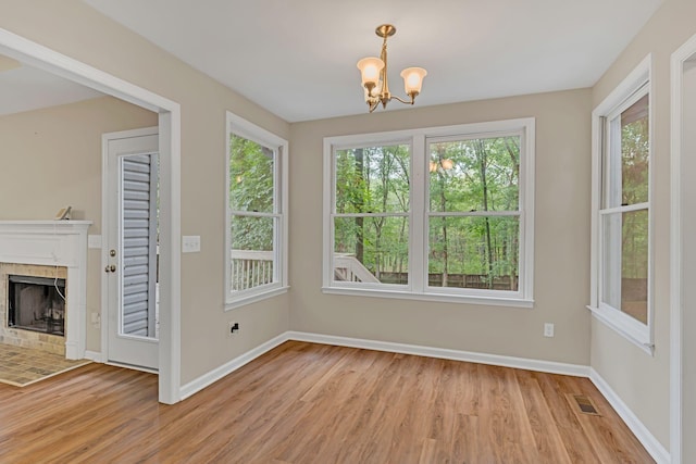 unfurnished dining area with a tiled fireplace, light hardwood / wood-style floors, and a chandelier