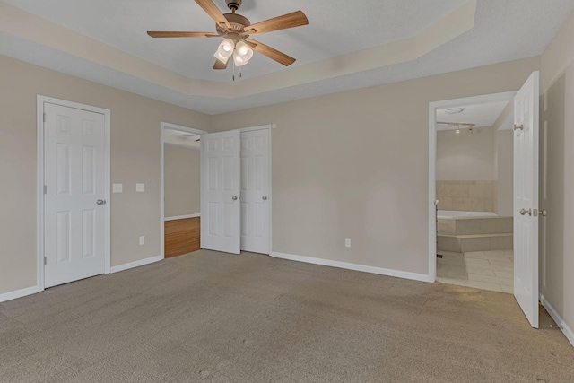 unfurnished bedroom featuring ensuite bathroom, carpet floors, ceiling fan, and a tray ceiling