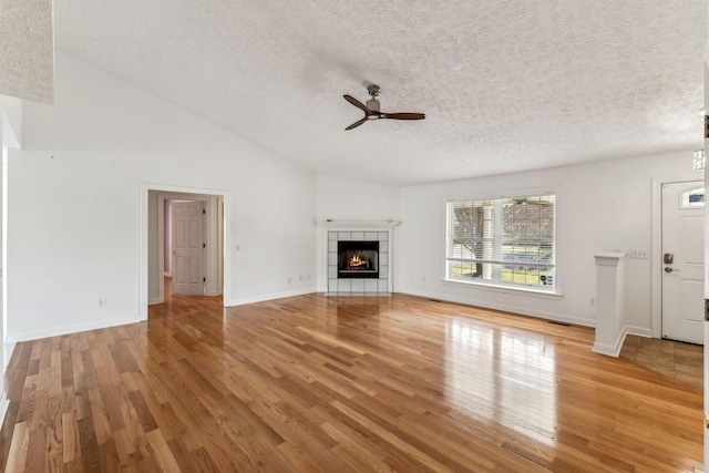 unfurnished living room featuring lofted ceiling, hardwood / wood-style flooring, ceiling fan, a textured ceiling, and a tiled fireplace