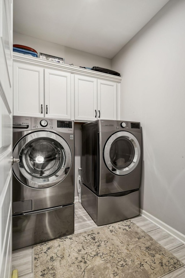 washroom with cabinets, washer and dryer, and light hardwood / wood-style flooring