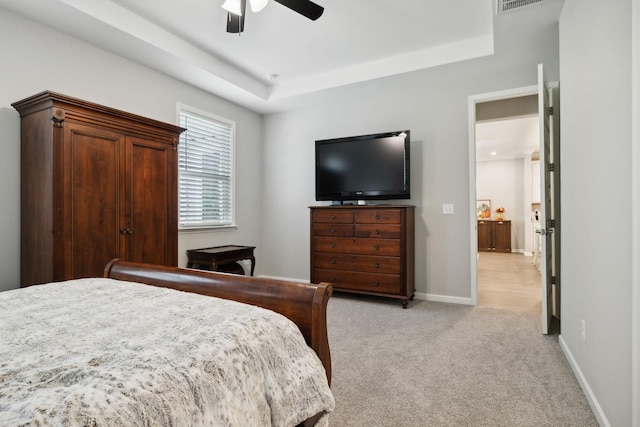 bedroom with light carpet, a tray ceiling, and ceiling fan