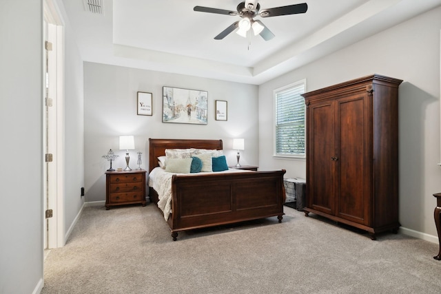 bedroom featuring ceiling fan, a tray ceiling, and light carpet