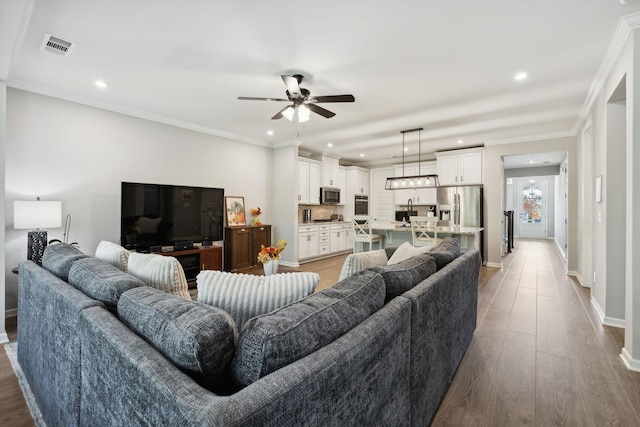 living room with ceiling fan, ornamental molding, and light hardwood / wood-style floors