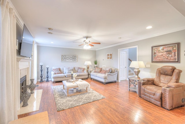 living room with hardwood / wood-style flooring, ceiling fan, ornamental molding, and a high end fireplace