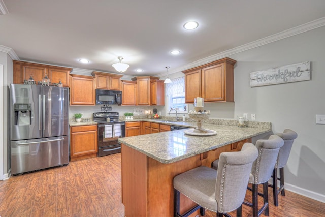 kitchen featuring hanging light fixtures, light wood-type flooring, ornamental molding, kitchen peninsula, and black appliances