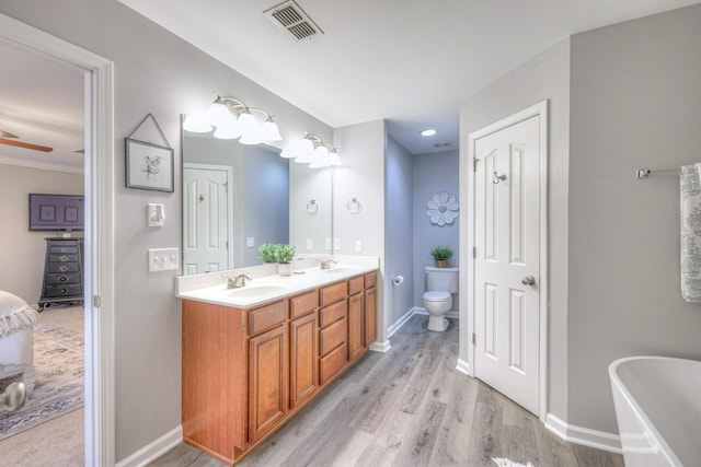 bathroom featuring ceiling fan, hardwood / wood-style floors, vanity, a tub, and toilet