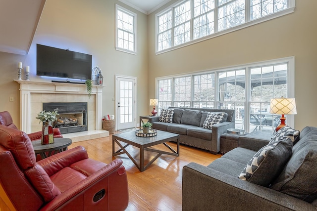 living room with a tile fireplace, ornamental molding, light hardwood / wood-style floors, and a towering ceiling