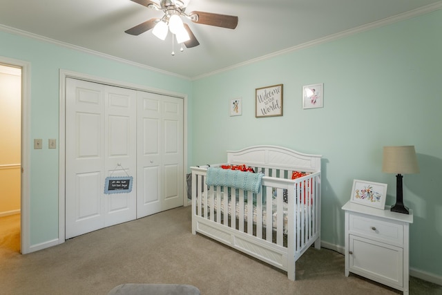 carpeted bedroom featuring ceiling fan, ornamental molding, a closet, and a crib