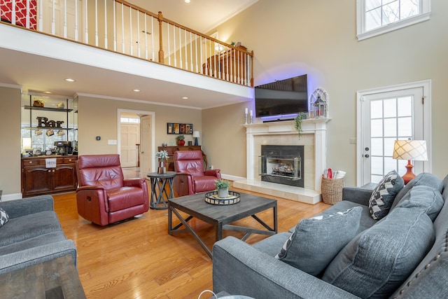 living room featuring ornamental molding, a healthy amount of sunlight, light hardwood / wood-style floors, and a towering ceiling