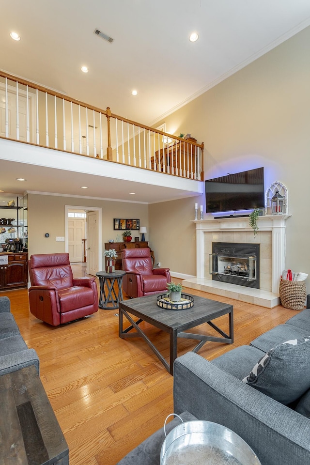 living room with a tiled fireplace, ornamental molding, a high ceiling, and hardwood / wood-style floors