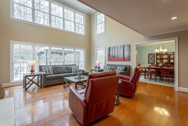 living room with crown molding, a towering ceiling, an inviting chandelier, and light hardwood / wood-style flooring