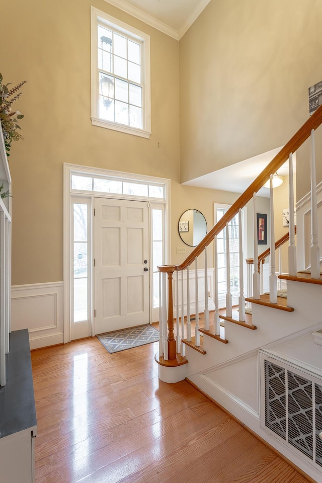 foyer with a towering ceiling, a wealth of natural light, ornamental molding, and light hardwood / wood-style floors