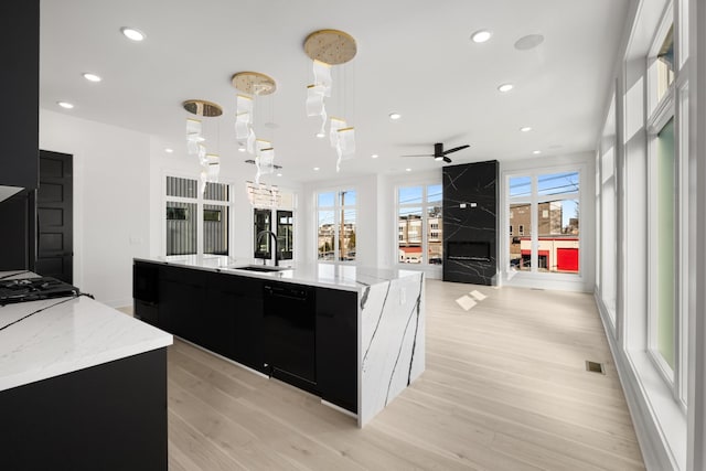 kitchen with pendant lighting, black dishwasher, sink, a large island, and light hardwood / wood-style floors