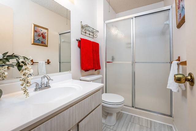 bathroom featuring vanity, toilet, a shower with door, and a textured ceiling